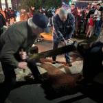 Randy Flink (left) and Abe Singer (not in photo) use a crosscut saw to cut the annual Festival of Lights Yule Log at Fleet Park under the guidance of Al Jones (middle) and Ron Lofgren (right).