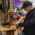 KTMK Gloves founder Ken Ervin slowly guides the outer shell of a catchers mitt through a sewing machine as he puts new leather edge bindings on the mitt as part of glove restoration for a customer.