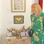 Marguerite Garth of Tokeland was one of the curators. Her work included a painting of President Trump as if in The Scream, a guitar sculpted from wood and found objects inspired by the song Alligator Alcatraz, and a three-dimensional exhibit whose title translates as who will guard the guardians? drawing on her fascination with the It draws on her fascination with the ancient Book of Kells in Ireland.